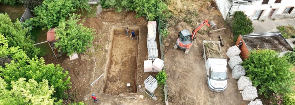 Chantier de construction aérien: excavation de piscine, ouvriers, pelleteuse orange chargeant un camion Jardin Vert, matériaux.