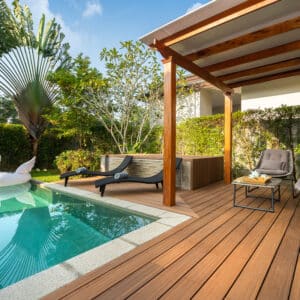 Piscine privée et terrasse en bois avec transats et coin salon sous pergola dans un jardin tropical luxuriant.