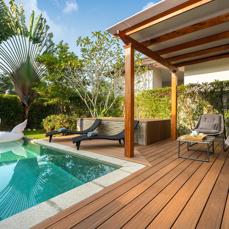 Piscine privée et terrasse en bois avec transats et coin salon sous pergola dans un jardin tropical luxuriant.